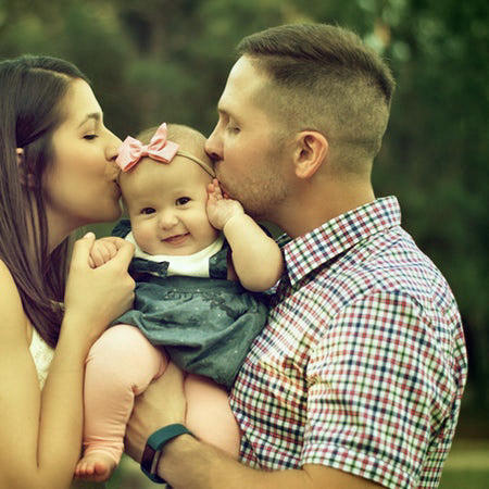 Photo of an attractive young couple kissing their baby daughter between them.