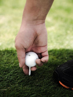 Man's hand placing golf ball on tee in the grass